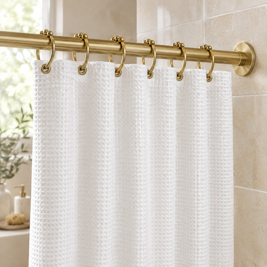 Rideau de douche blanc gaufré suspendu à une tringle dorée par des anneaux de rideau de douche en métal doré
